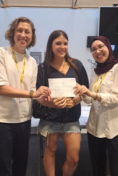 A student from The King Alfred School Sixth Form stands between two teachers, holding her A level exam results card