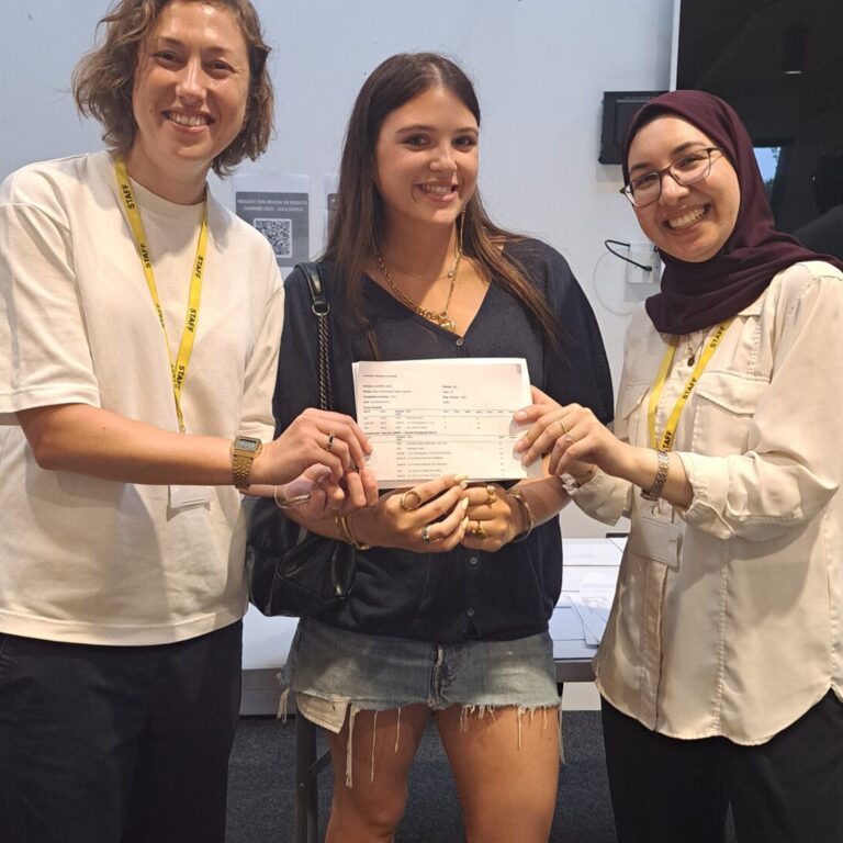 A student from The King Alfred School Sixth Form stands between two teachers, holding her A level exam results card