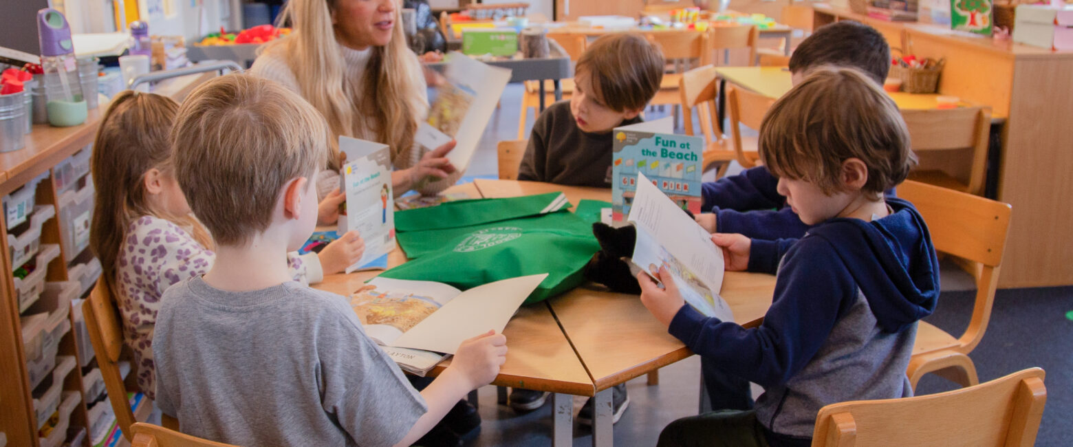Young children read at a desk with a teacher