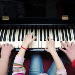 three pairs of hands playing a piano