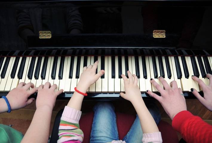 three pairs of hands playing a piano