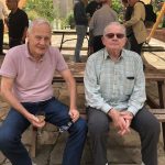 two elderly gentlemen sitting on a bench drinking wine