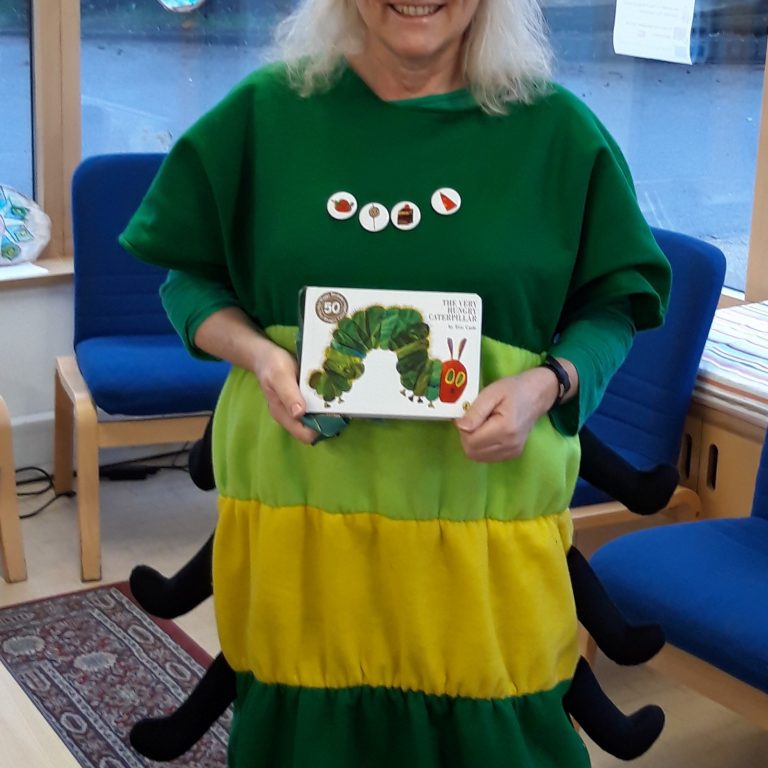 Woman wearing a caterpillar costume holding 'My Very Hungry Caterpillar'
