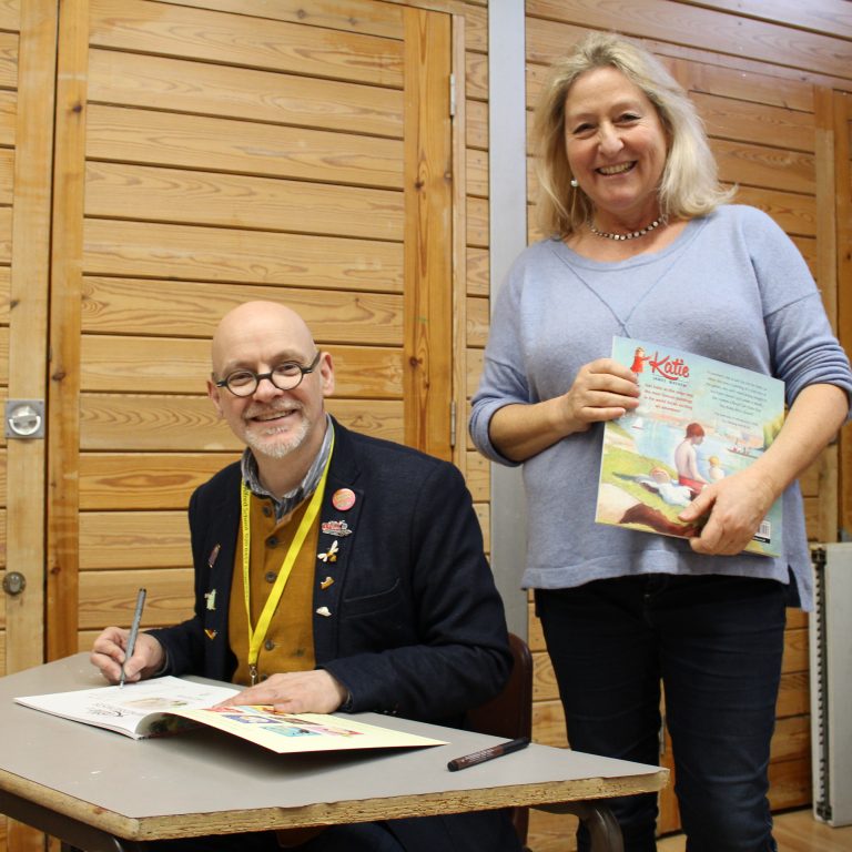 Two members of staff holding and writing in a picture book