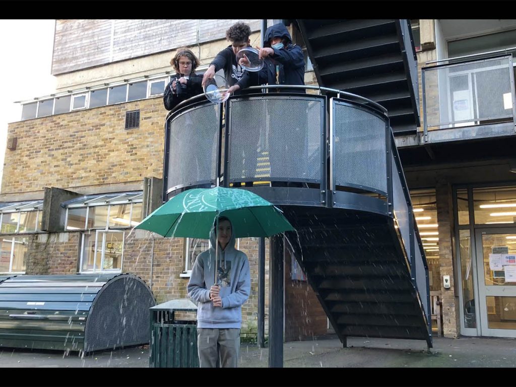 Sixth form students shooting a film, pouring water on an umbrella