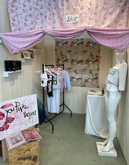 Pink floral curtain, mannequin, clothes rack with clothes hanging from it, and artwork