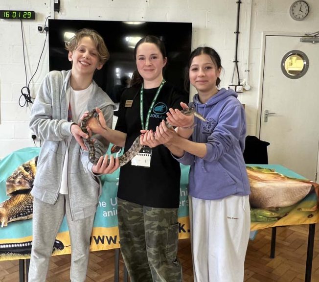 students and visitor holding a snake