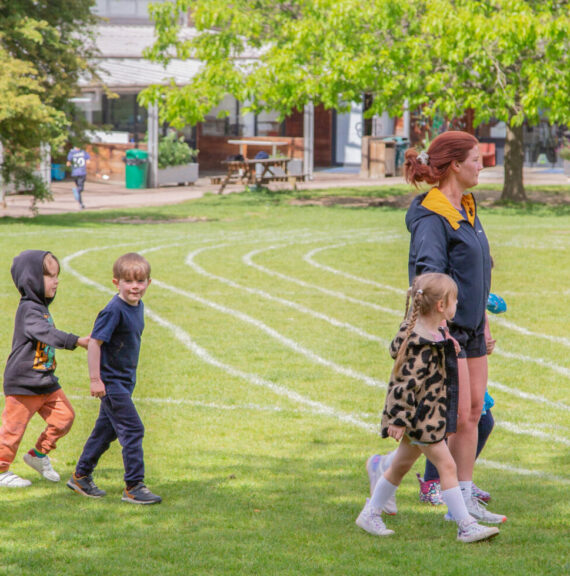 Lower School students from The King Alfred School in Hampstead walk across a field marked with athletics tracks alongside a teacher