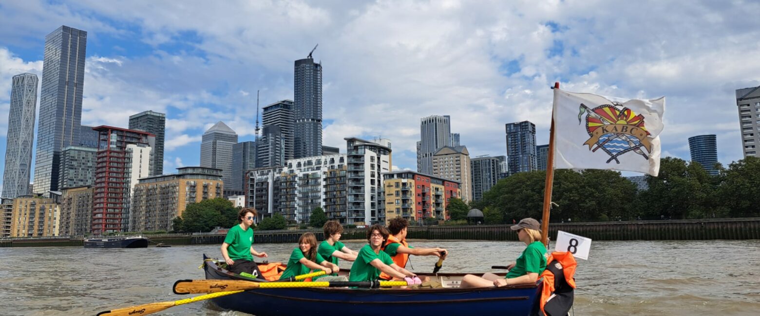 Students from The King Alfred School Sixth Form pictured rowing a boat along the Thames, with Canary Wharf in the backrground