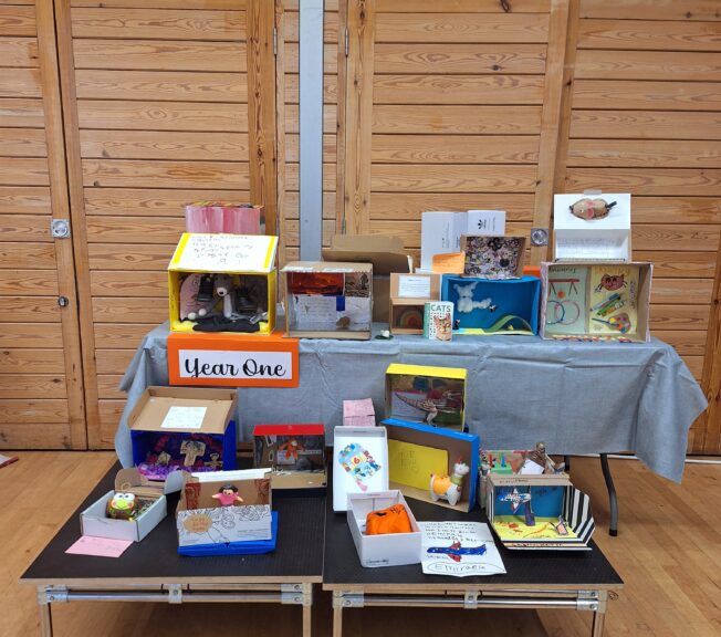 A selection of colourfully decorated shoeboxes on a high and low table, with a sign that reads 'Year One'.