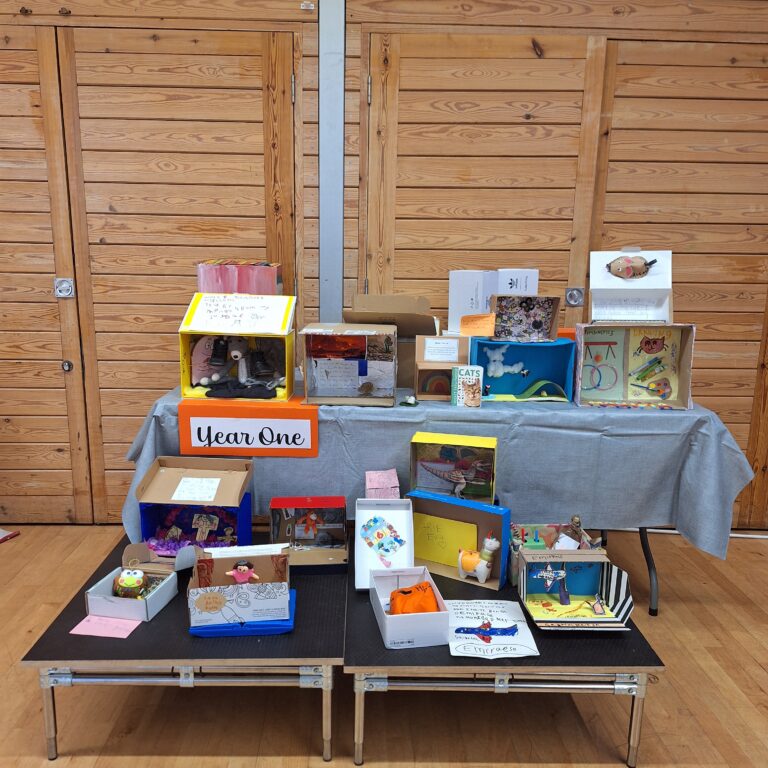 A selection of colourfully decorated shoeboxes on a high and low table, with a sign that reads 'Year One'.