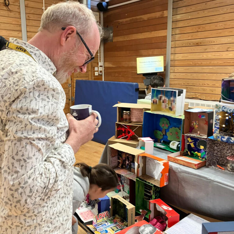 A man smiles as he takes in a display of decorated shoeboxes, with a young girl leaning in for a closer look