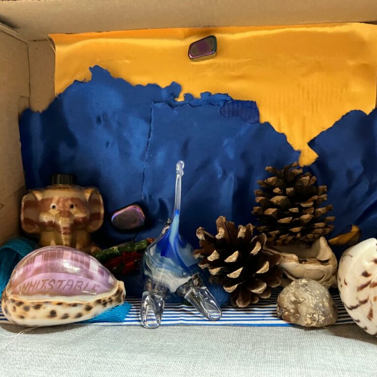 A shoebox on its side, painted blue and orange and decorated with shells and pinecones.