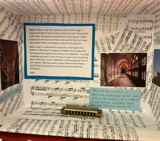 A shoebox on its side decorated with sheets of music, a mouth organ and pictures of cathedrals. A note reads: 'When I was six my mum gave me this mouth organ. I loved working out how to play tunes on it and I discovered that I really enjoyed playing different instruments. Now I mostly play the piano and violin just for fun, but I have also taught music and played violin for folk dances. Now I sing in a cathedral touring choir, which goes to a different cathedral in England of Wales twice a year and we sing all the religious services for the weekend. It's a big challenge as there is lots of music to learn but I love being part of the choir. Every cathedral is interesting and has its own history. We have even sung in Westminster Abbey and St Paul's cathedral, but my favourite is Salisbury Cathedral.'