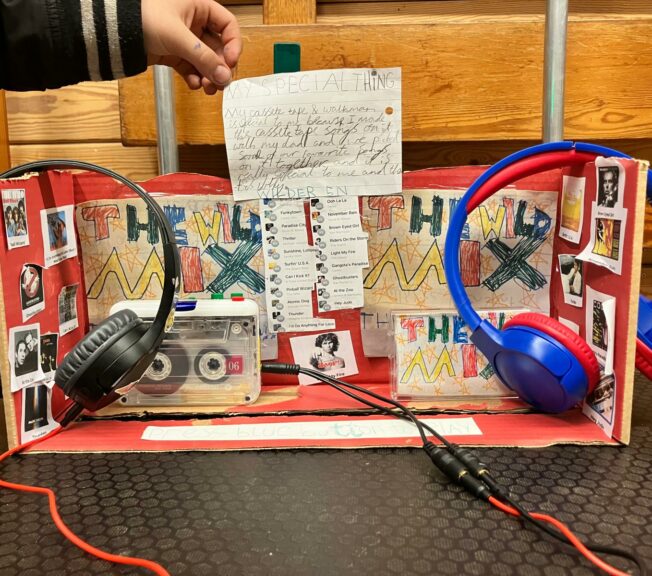 A decorated shoebox with a personal cassette tape player inside and two pairs of headphones attached. A playlist is stuck on the side, and a note reads: 'My Special Thing. My cassette tape and Walkman is special to me because I made the cassette tape songs on it with my dad and we picked some of our favourite songs on it together and it is really special to me and that is why.'