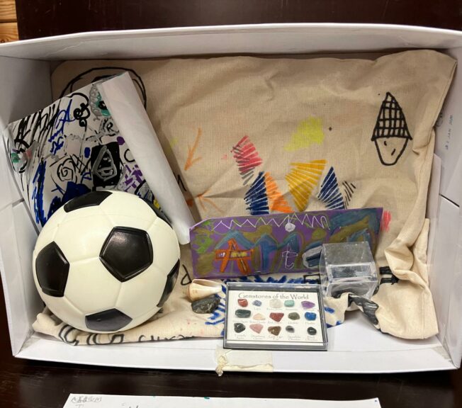 A shoe box on its side with drawings, a small football and a collection of crystals inside