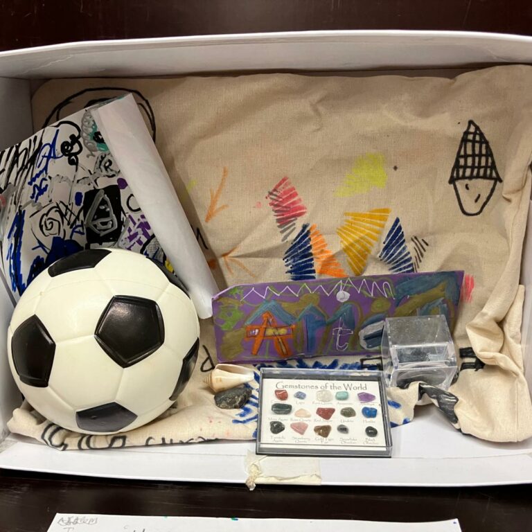 A shoe box on its side with drawings, a small football and a collection of crystals inside