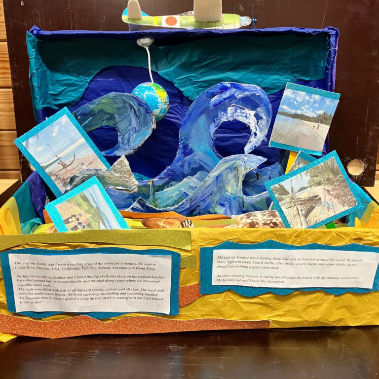 A shoebox painted blue and yellow to look like the beach and sea with waves. There are also shells and pictures of children on a beach, with a note that reads: 'This year my family and I went travelling around the world for four moths. We went to Costa Rica, Panama, USA, California, Fiji, New Zealand, Australia and Hong Kong. During our travels my brother and I loved finding shells like these on the tropical beaches.'
