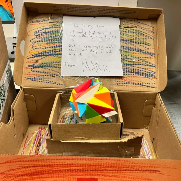 A decorated shoebox with a puzzle block inside. A note reads: 'This is my cube, it's really hard to solve and actually I can't solve it. But I keep trying and I know one day I will solve it.'