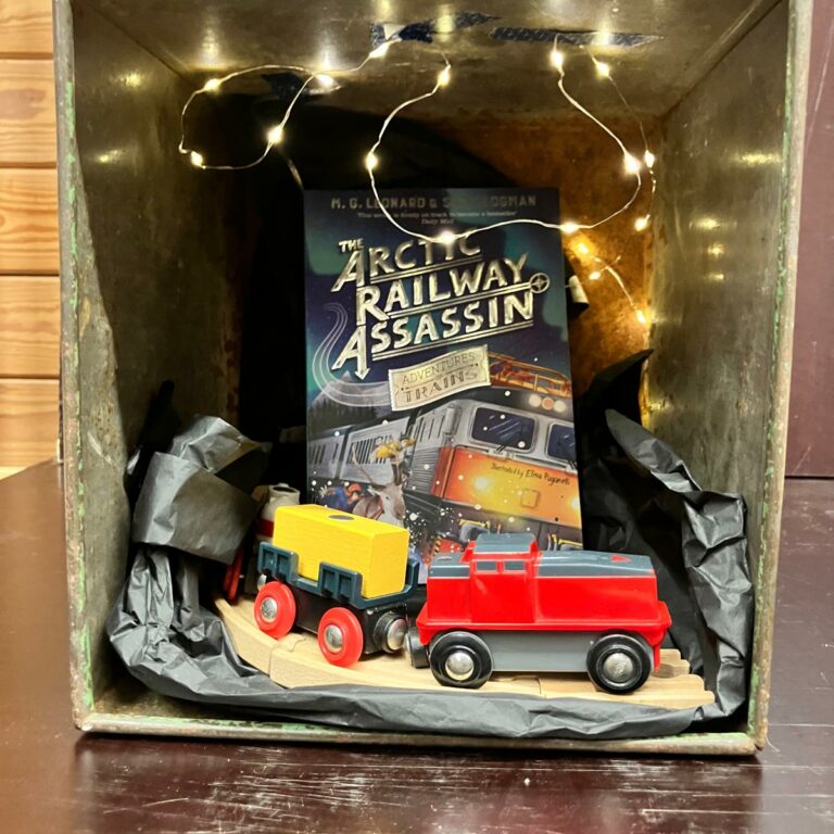 A box decorated inside with fairy lights and a wooden train. There is also a copy of the book The Arctic Railway Assassin.