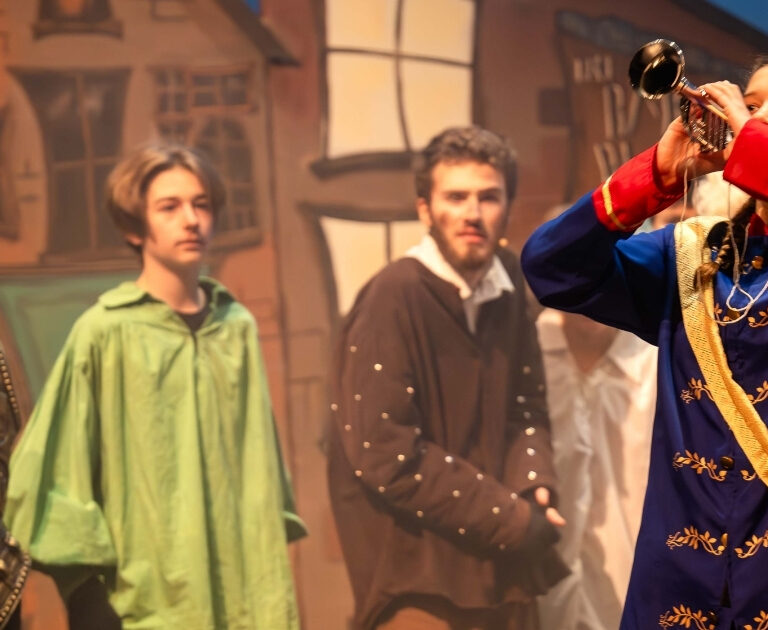 Actor in The Ballad of Raggedy Alice blows a trumpet, as other characters look on