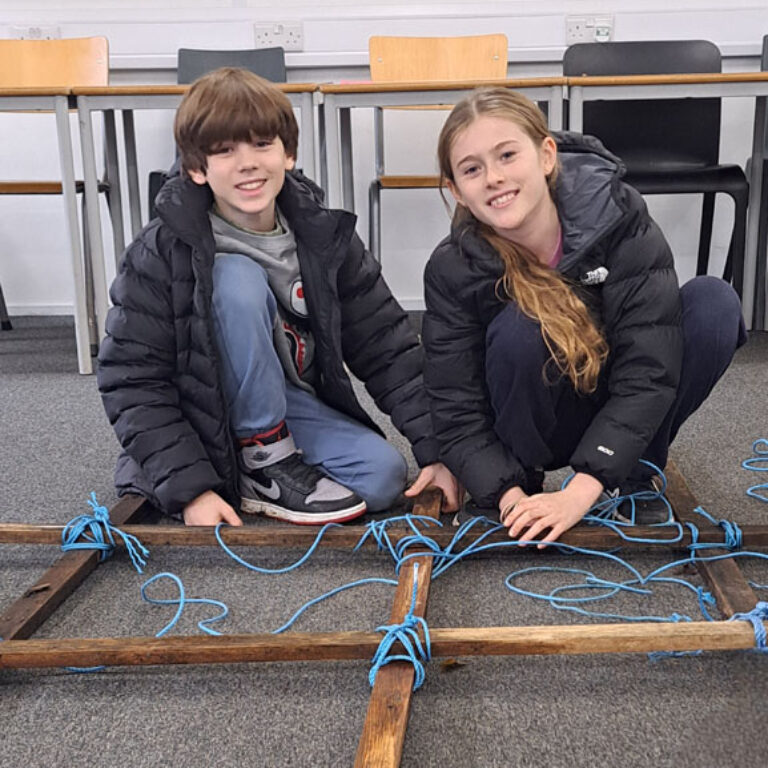students lash together wood to create a shelter