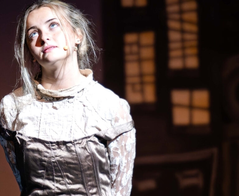 A female actor looks wistfully upwards whilst on stage