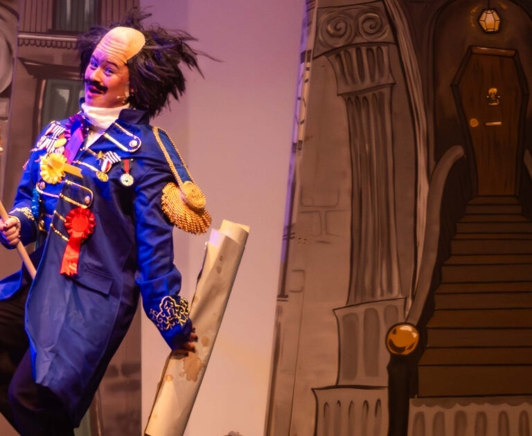 An actor rides a Hobby Horse, sporting a comical expression