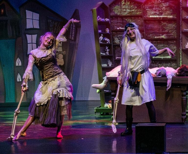 Two female actors dance with bone props on stage