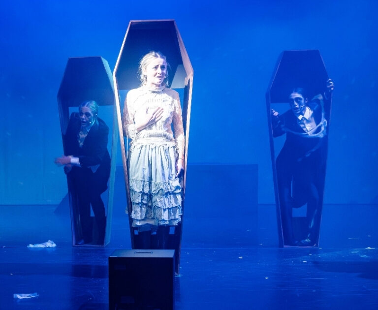 Actors perform inside coffins stood up on stage