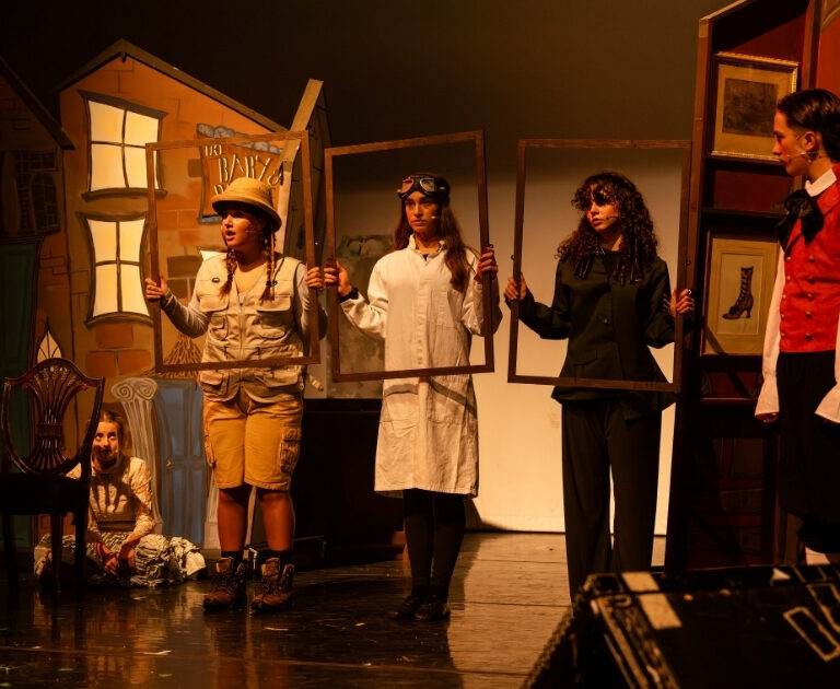 Three performers hold empty picture frames on stage