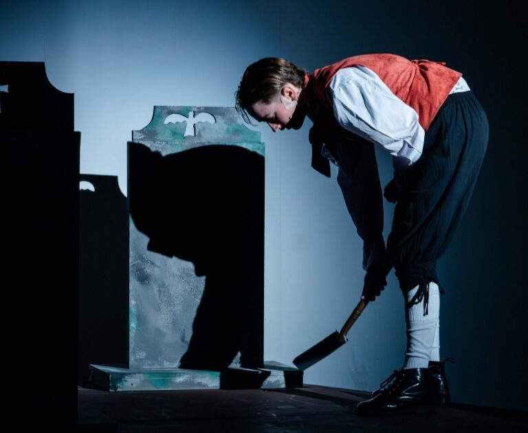 An actor is seen digging a grave on stage
