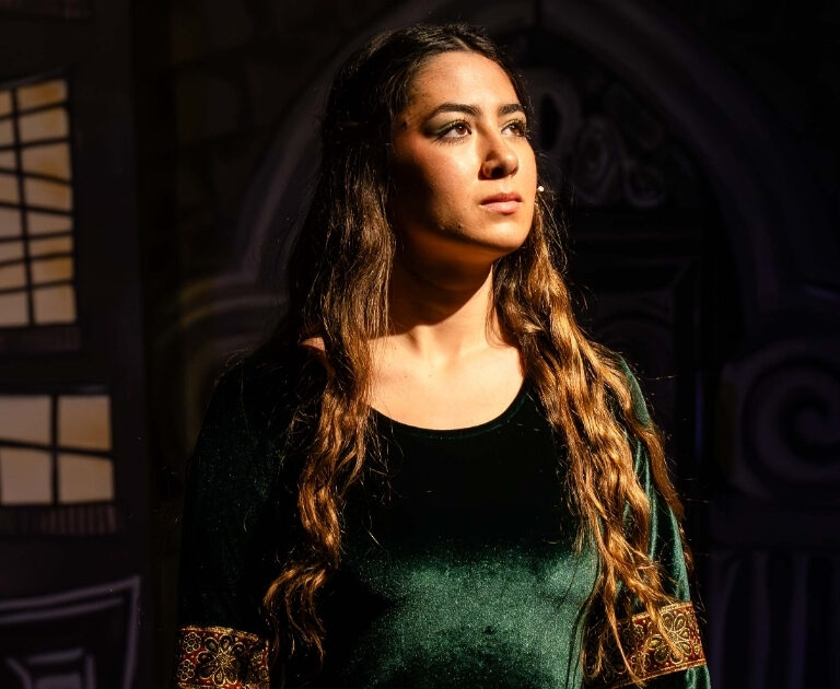 A female actor with long dark hair and wearing a green velvet dress