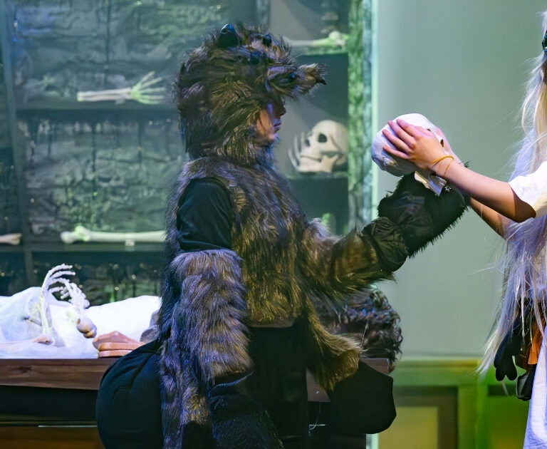A performer dressed as a scientist taking a skull from a giant spider