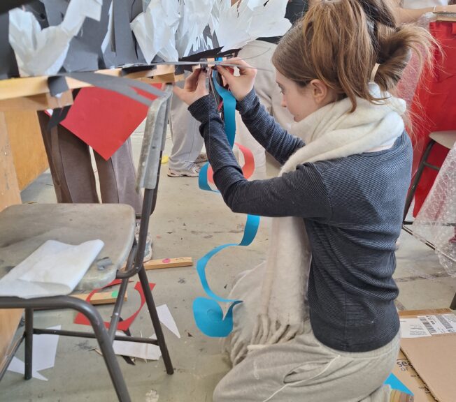 A student from The King Alfred School attaches a spiral of blue paper to a wooden structure