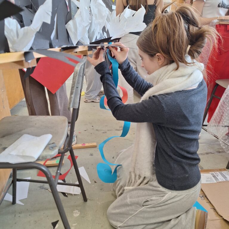 A student from The King Alfred School attaches a spiral of blue paper to a wooden structure