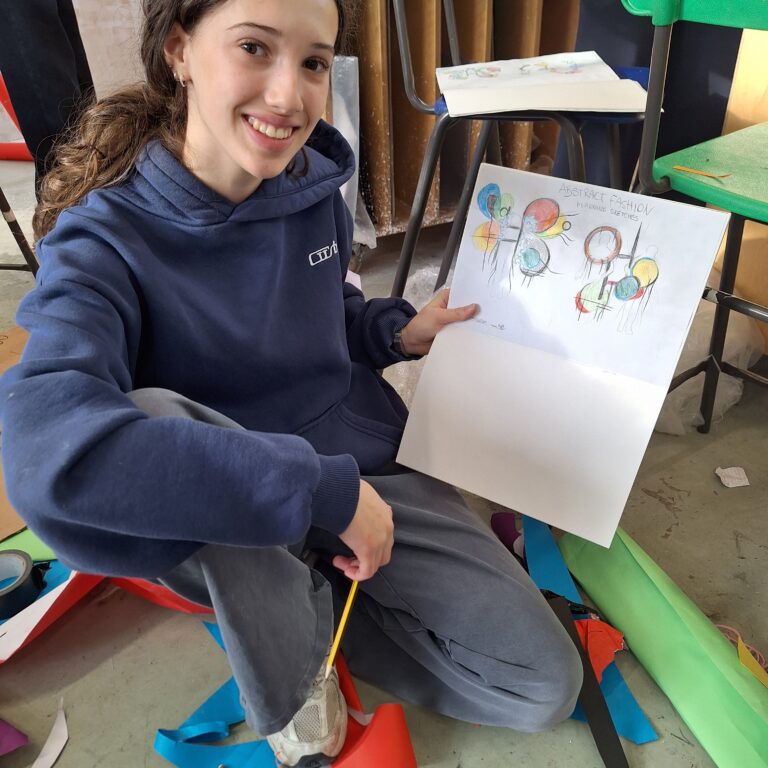 A student smiles as she holds up a sketch of her abstract fashion design
