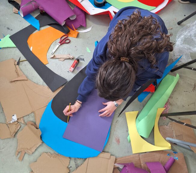A student kneels on the floor surrounded by colourful paper and card in the art room at The King Alfred School