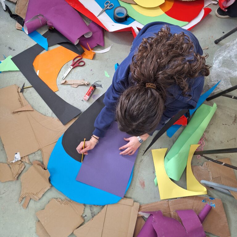 A student kneels on the floor surrounded by colourful paper and card in the art room at The King Alfred School