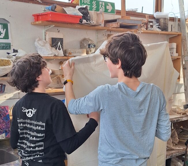Two male students at The King Alfred Scholl attach a piece of material to a wooden frame