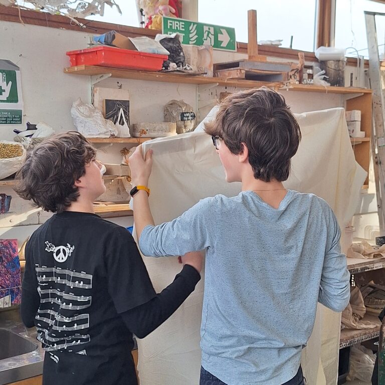 Two male students at The King Alfred Scholl attach a piece of material to a wooden frame