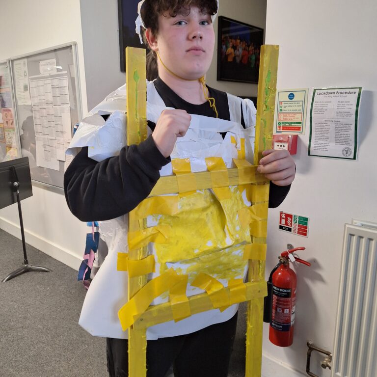 A male student wears a white tabard with strips of yellow paper across the front, giving the illusion of a fried egg