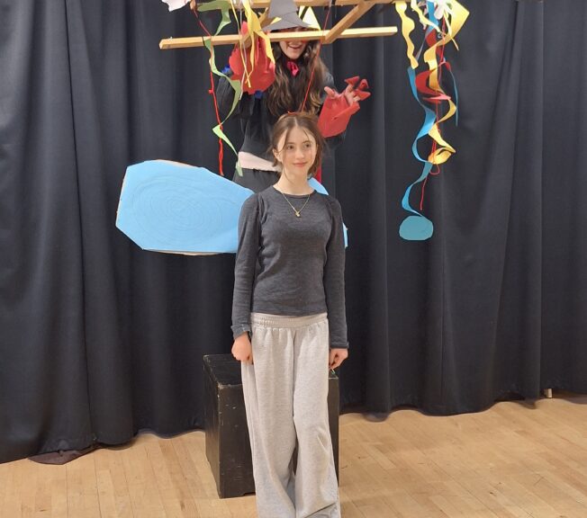 A student holding an abstract puppetry device, with her 'puppet' played by a fellow student