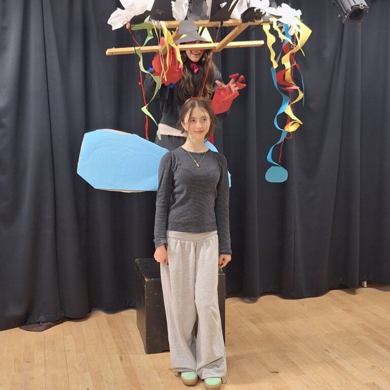 A student holding an abstract puppetry device, with her 'puppet' played by a fellow student