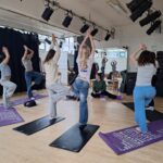 Female students perform tree pose on yoga mats in a bright and airy studio space