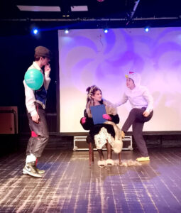 Three people perform on stage at The King Alfred School in strange costumes