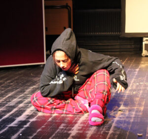 A student in tartan pyjama bottoms acts on stage as part of a clowning performance