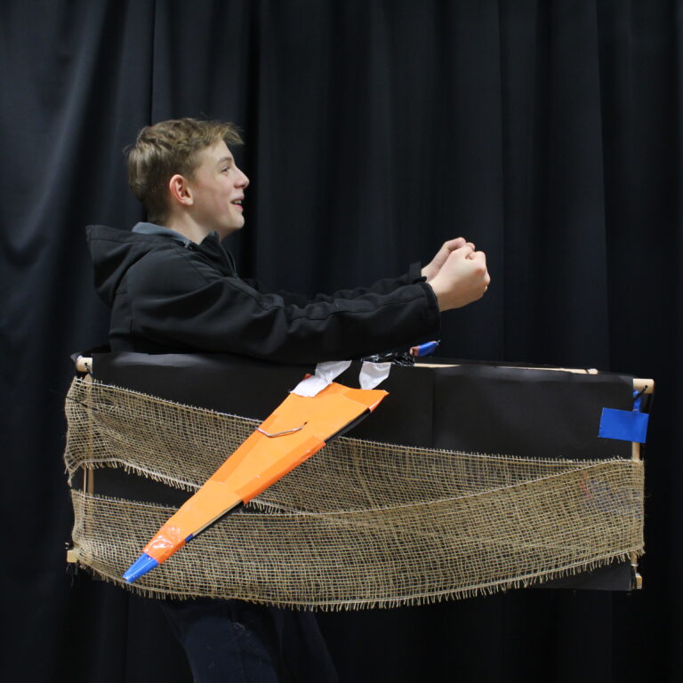 A student wearing a box shaped like a plane around his waist, with orange wings and a black body