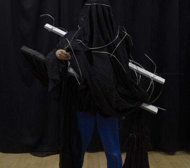 A student wears an abstract fashion design featuring a black cloak and silver wire