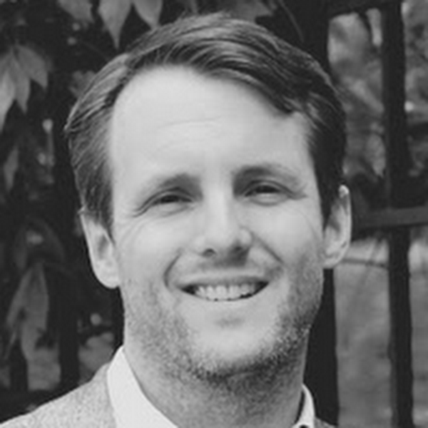 Black and white headshot of a white male in front of shrubs and a gate